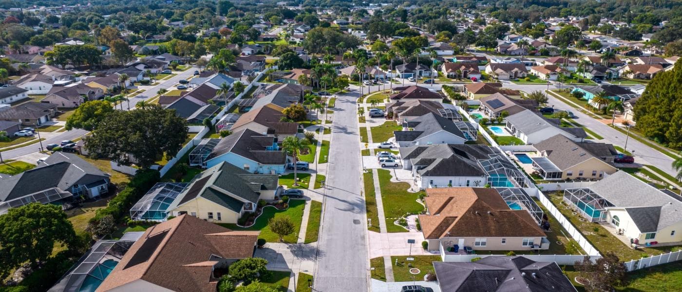 Aerial view of a sunny suburban neighborhood with houses, swimming pools, and palm trees.